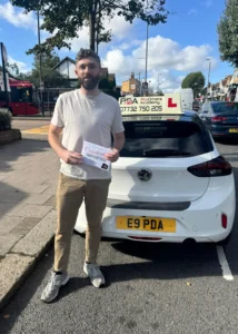 Cormac celebrating after passing his manual driving test outside Chingford Test Centre beside the learner car.