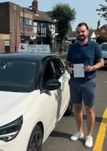 Florin celebrating after passing his manual driving test outside Chingford Test Centre beside the learner car with Pro Drivers Academy